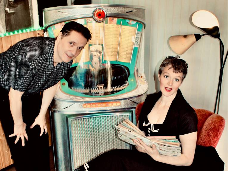 Eine Frau und ein Mann neben einer Jukebox im Stil der Fünfzigerjahre.